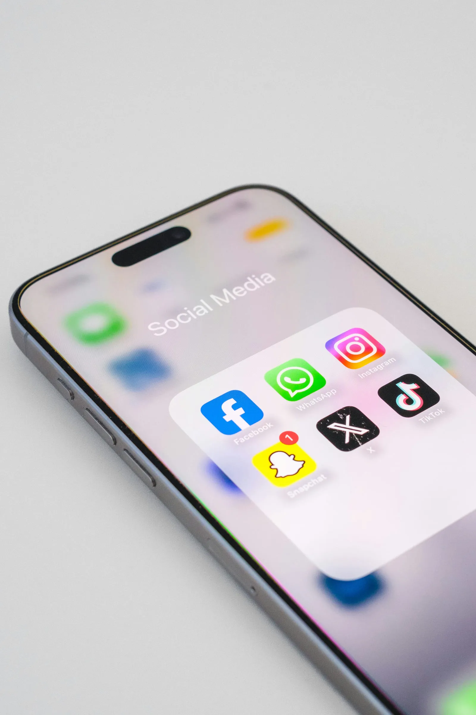 Smartphone mit geöffnetem Ordner „Social Media“: Facebook, WhatsApp, Instagram, TikTok, X und Snapchat nebeneinander.